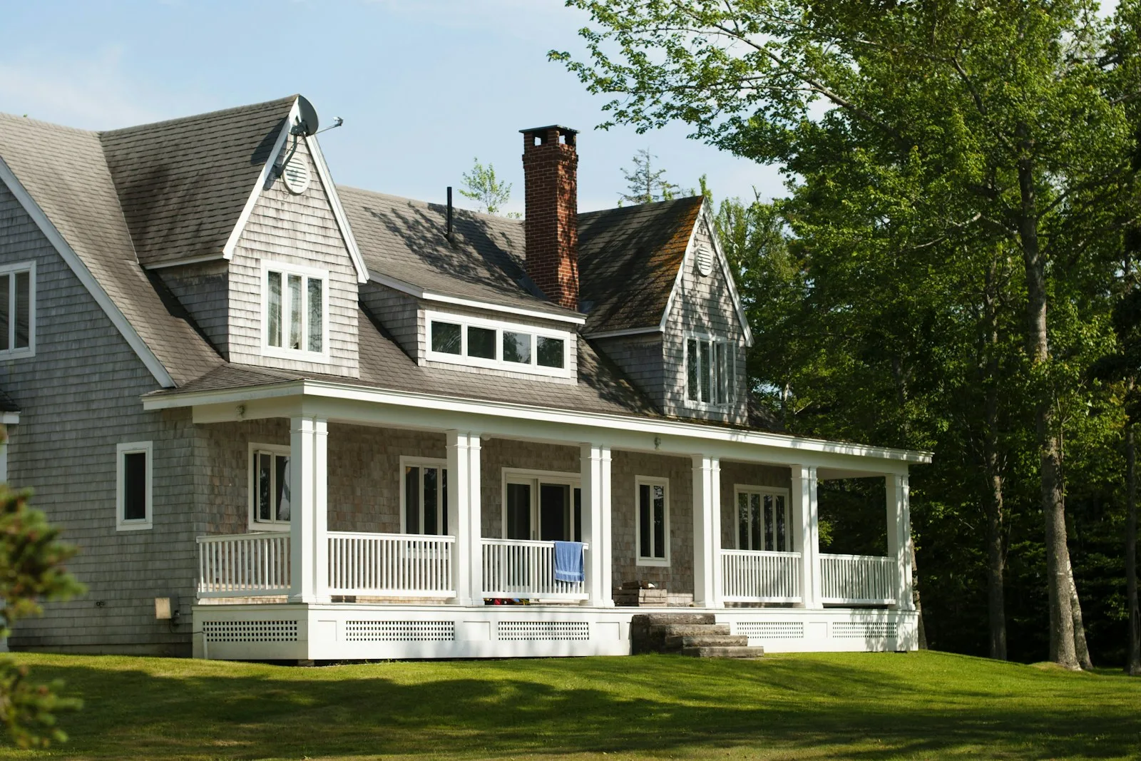Gray shingled New England home with a white columned porch and mature trees
