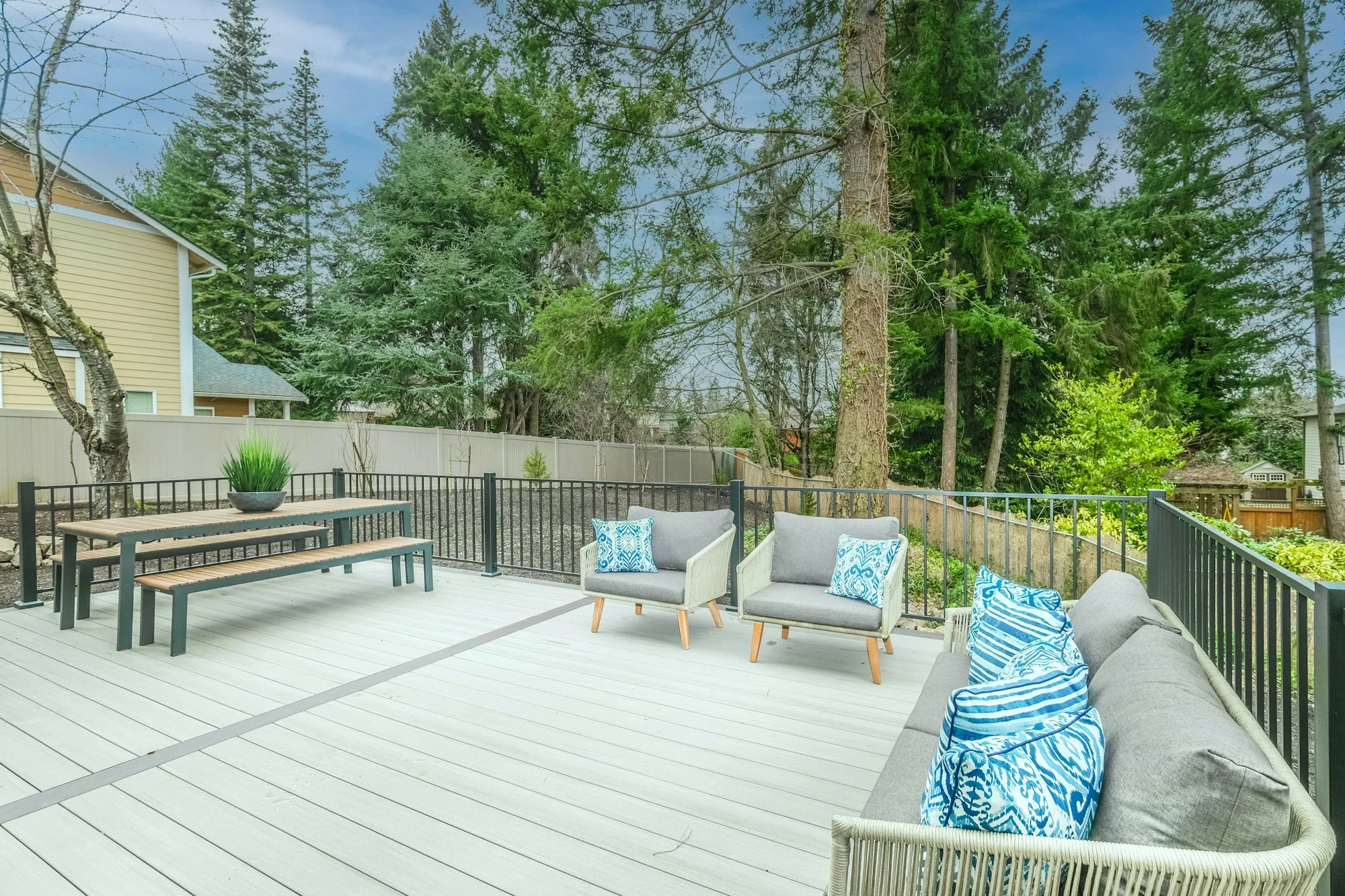 Gray composite deck with built-in bench seating and cushions, looking out over a wooded back yard