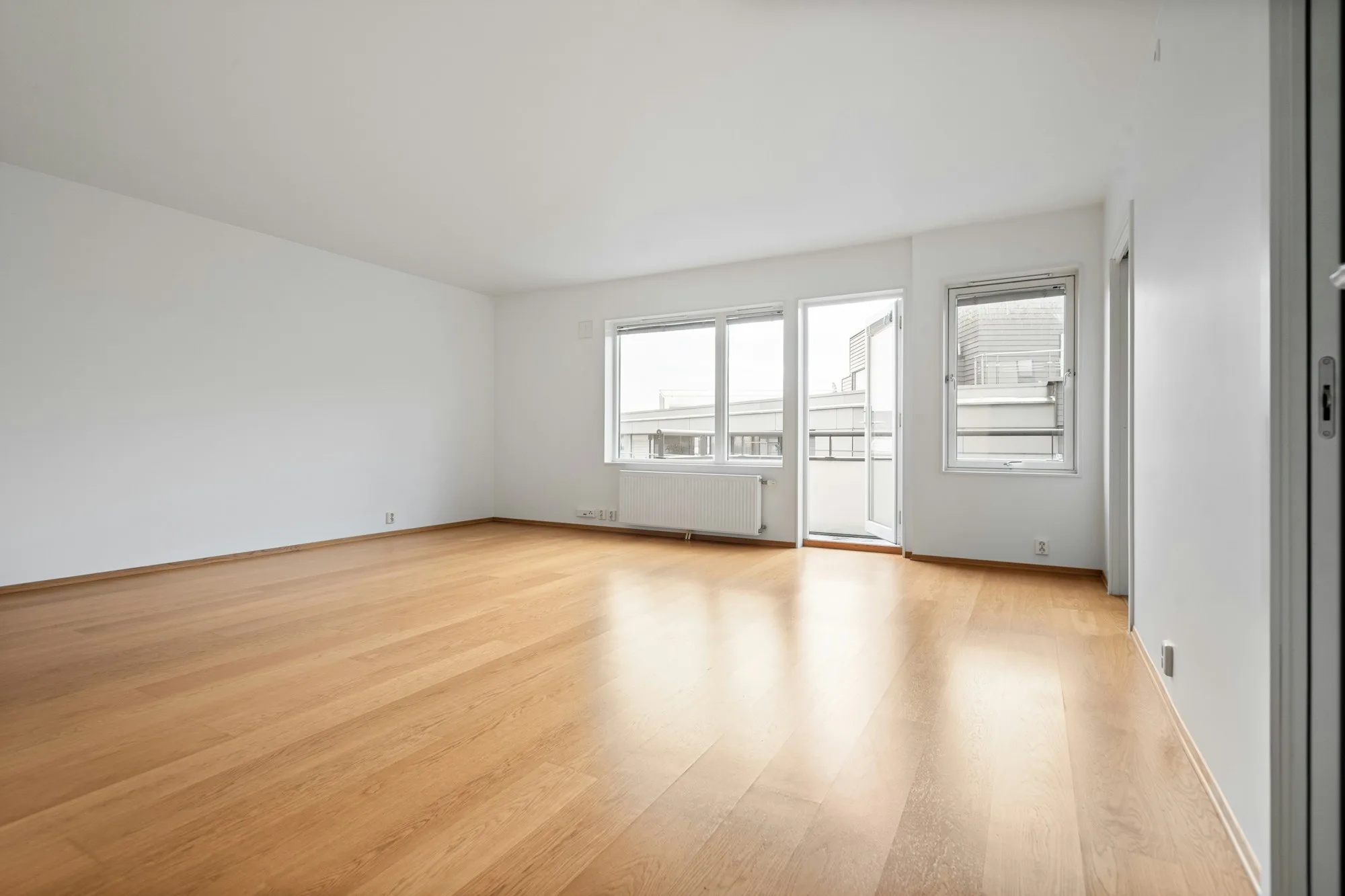 Finished empty room with an oak floor, white walls and daylight from a sliding glass door