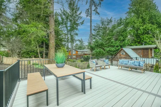 Table and chairs on a gray composite deck with a planter and a fenced wooded yard behind